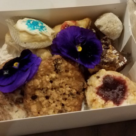 Takeaway box with various varieties of cookies and two purple and black pansies.